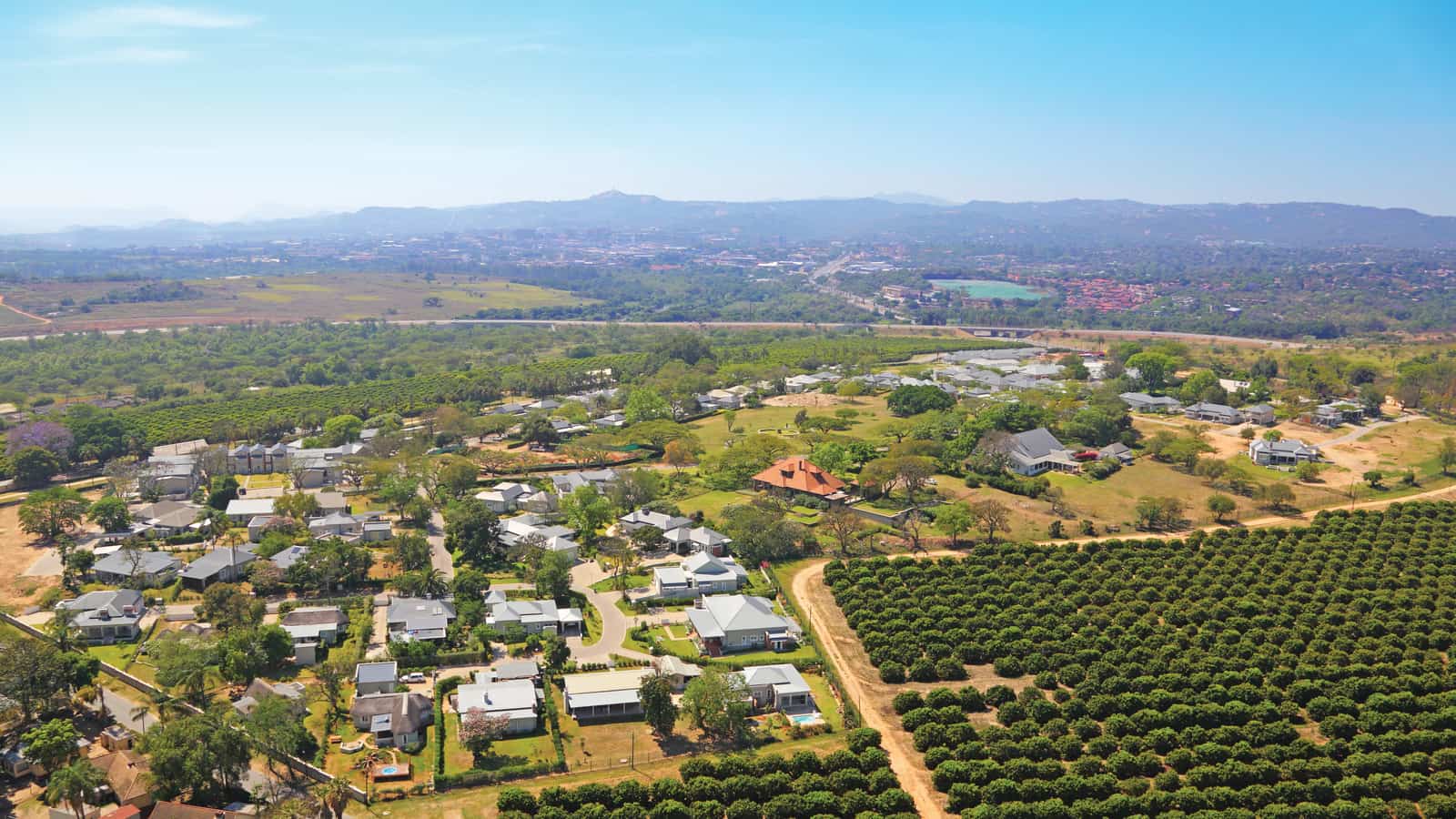 An aerial view of Mataffin: a residential estate of homes and gardens set among orchards, with the town and hills beyond